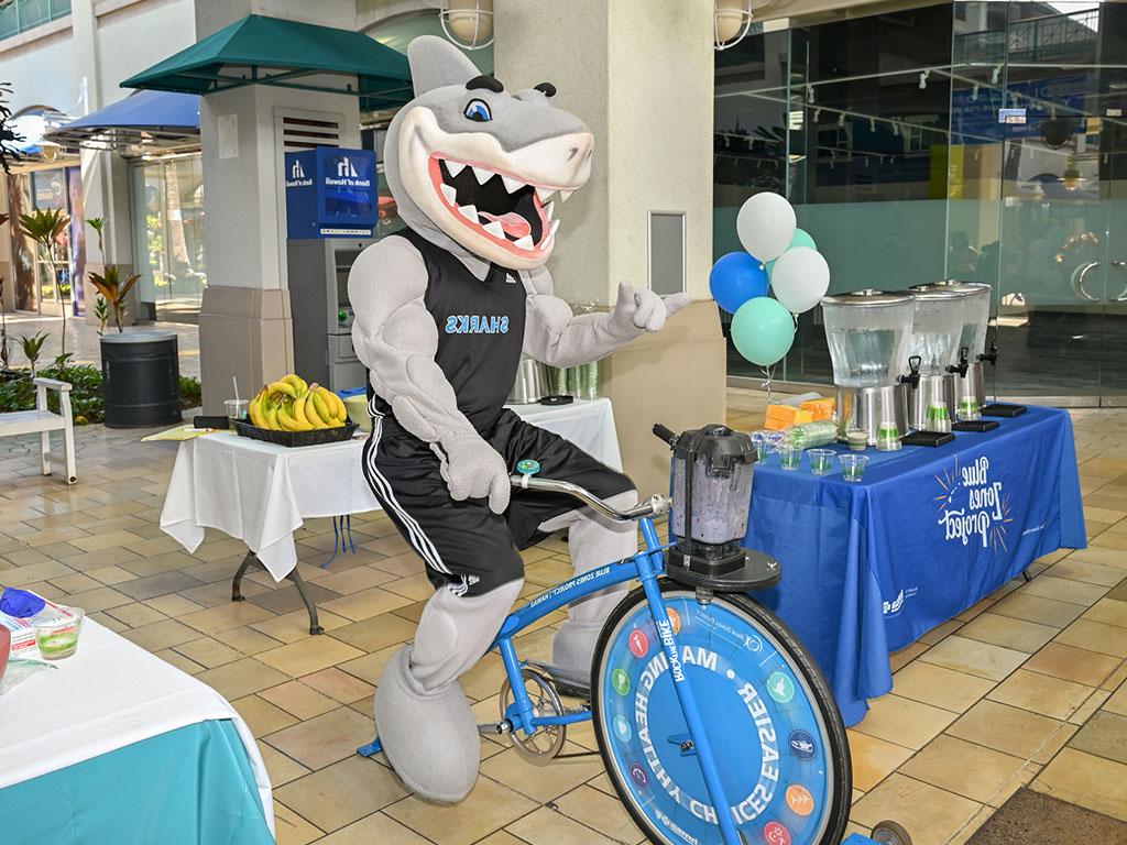 Sharky rides the blender bike at the celebration event at Aloha Tower Marketplace